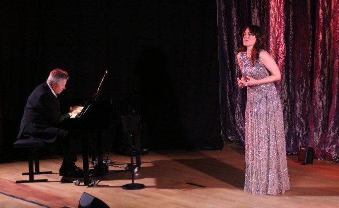 en kvinna i klänning på en scen med en man som spelar piano